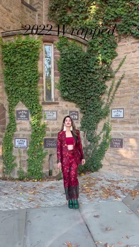 Roopsi Bansal in a burgundy floral suit standing in front of an ivy-covered stone building with class reunion plaques, with a '2022 Wrapped' text overlay