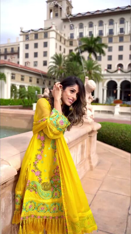 Roopsi Bansal in a yellow embroidered kurta set with a matching dupatta, leaning against a stone fountain ledge at The Breakers Palm Beach