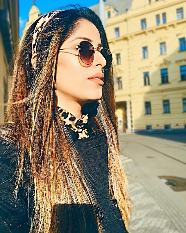 Standing on a sunny street wearing a leopard-print headband and scarf with a teal coat