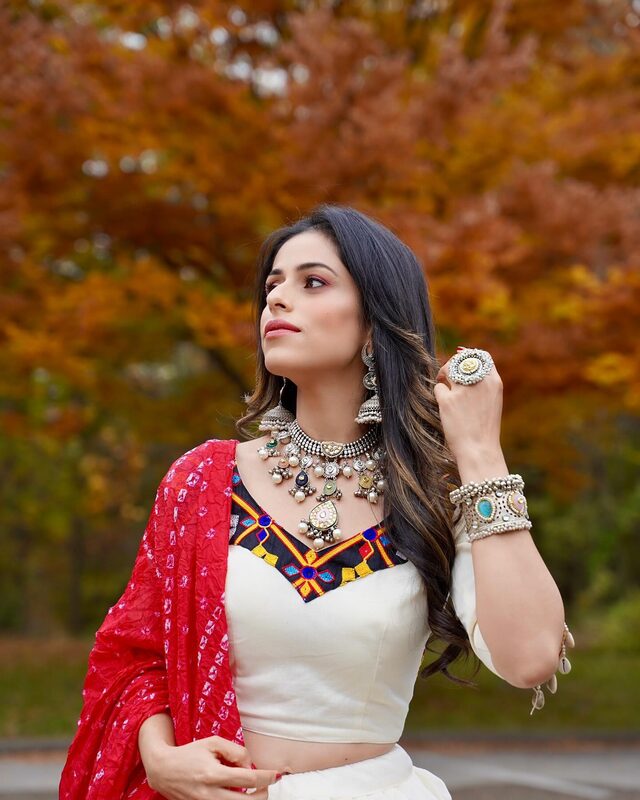 Roopsi Bansal in layered silver oxidized jewelry from Divakaari and an embroidered outfit from Glamour Indian Wear USA in front of fall foliage
