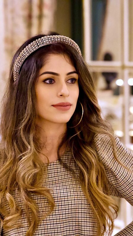 Close-up of Roopsi Bansal in a checked long-sleeve top with a jeweled headband, indoors at an elegant tea setting