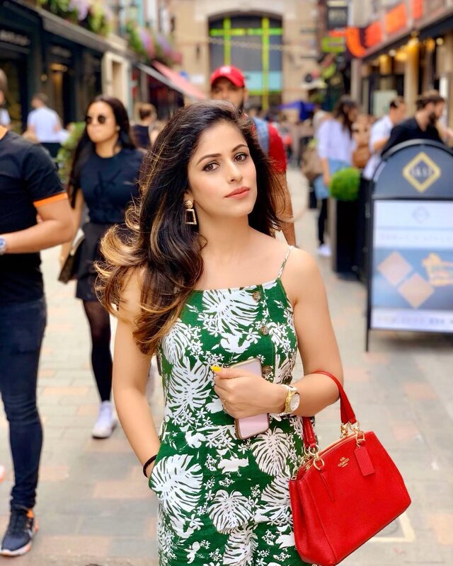 Walking a bustling Soho street in a green and white tropical-print sundress, gold drop earrings, and a red Coach handbag