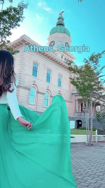 Roopsi Bansal in a white top and mint green chiffon maxi skirt from Chicwish, seen from behind with the skirt billowing out, facing the Athens City Hall clock tower