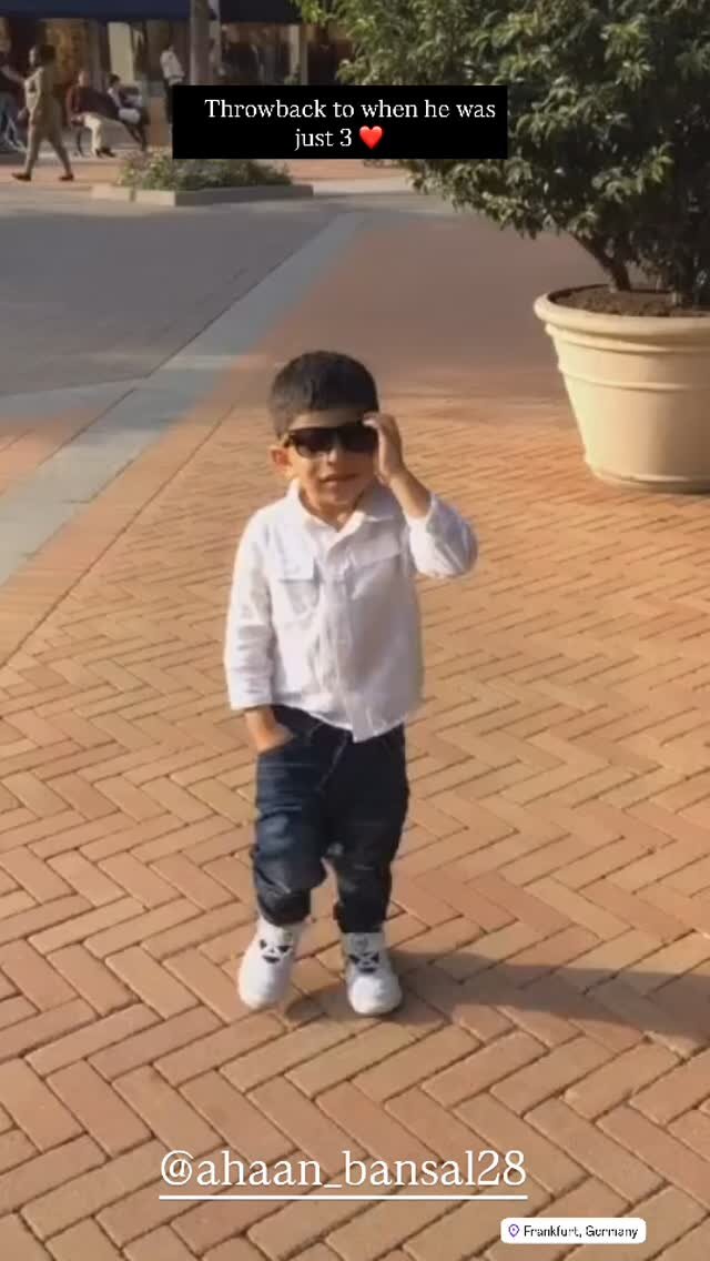 A young boy in sunglasses, a white shirt, and jeans walking a herringbone brick plaza in Frankfurt, Germany