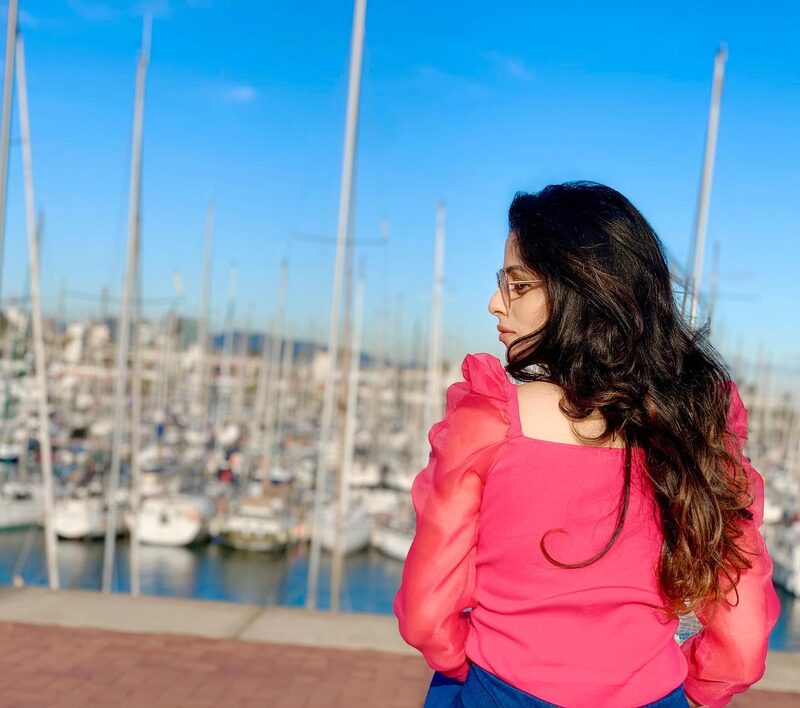 Standing at a Barcelona marina in a pink puff-sleeve blouse, looking out over a forest of sailboat masts at golden hour