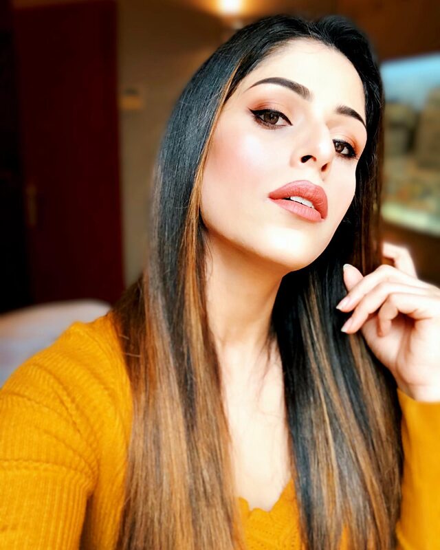 Close-up selfie with warm bronze eyeshadow and a matte orange-red Pat McGrath lipstick, wearing a mustard sweater indoors