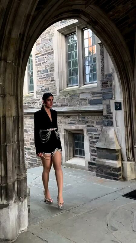 Roopsi Bansal in a black blazer dress with a crystal chain waist standing under a Gothic stone archway at Princeton