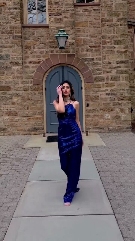 Roopsi Bansal in a royal blue satin gown and statement necklace standing in front of a stone archway doorway