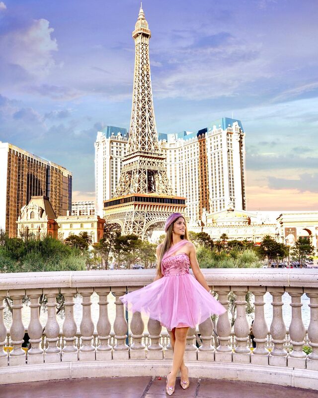Roopsi Bansal in a pink one-shoulder tulle dress and matching beret, standing on a balcony with the Eiffel Tower replica at Paris Las Vegas behind her