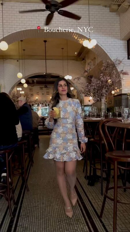Roopsi Bansal in a blue and cream floral lace dress holding a cocktail inside the French bistro Boucherie in New York