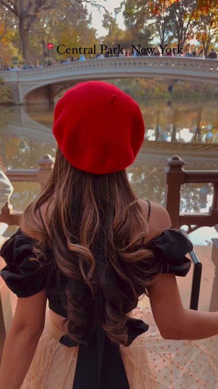 Roopsi Bansal in a red beret and black off-shoulder top in front of Bow Bridge in Central Park