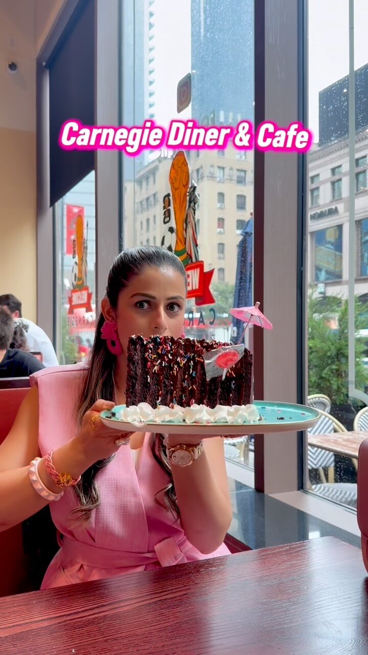 Roopsi Bansal at Carnegie Diner & Cafe holding up a tall slice of chocolate cake