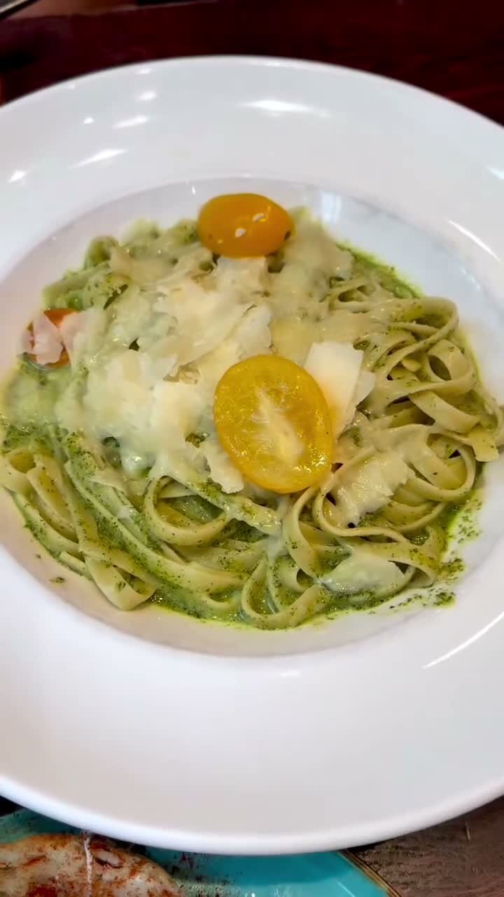 A plate of pesto fettuccine topped with shaved cheese and yellow cherry tomatoes