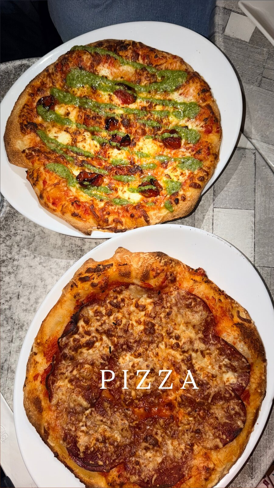 Two pizzas on white plates, one with pesto drizzle and sundried tomatoes, the other with seasoned meat and cheese, labeled PIZZA