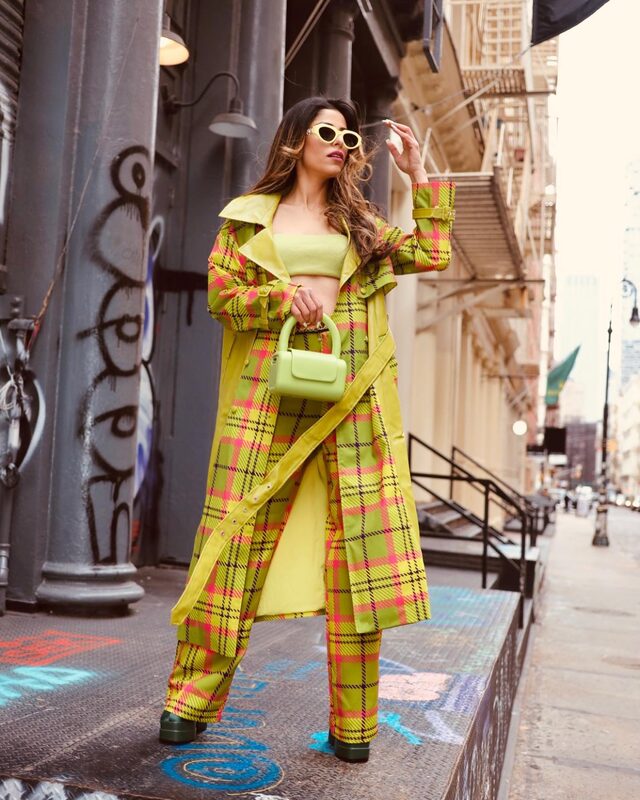 Roopsi Bansal in a chartreuse plaid trench coat and matching pants standing under a fire escape in Soho, New York