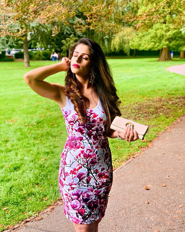 Roopsi Bansal in a cherry blossom print bodycon dress, standing on a path in a green London park