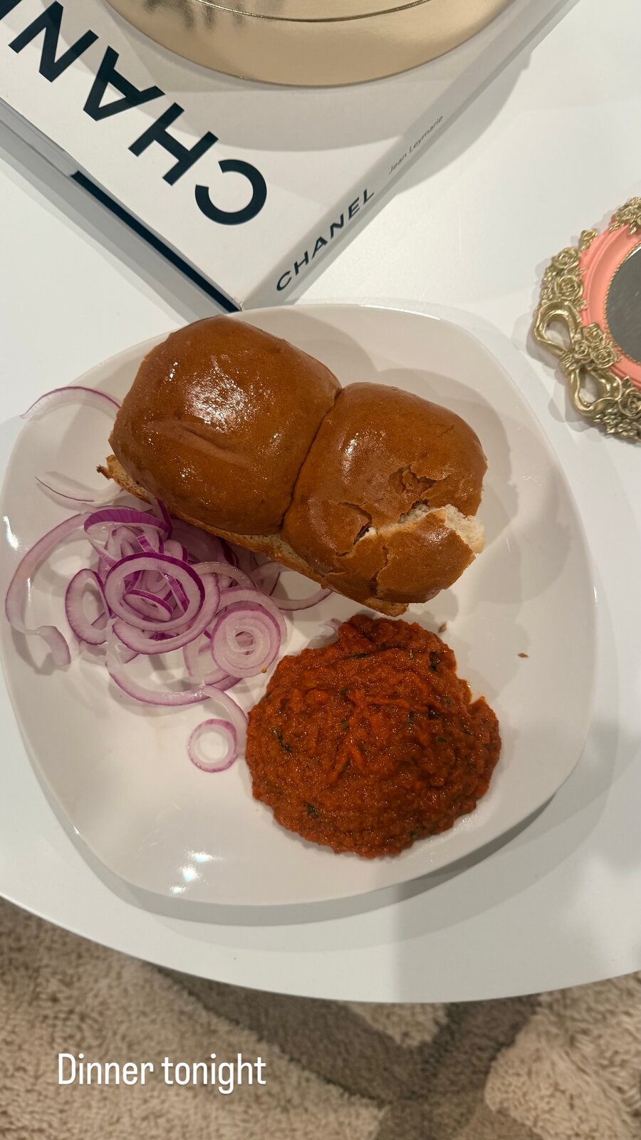 A plate with pav buns, sliced red onion and a fried patty beside a Chanel book