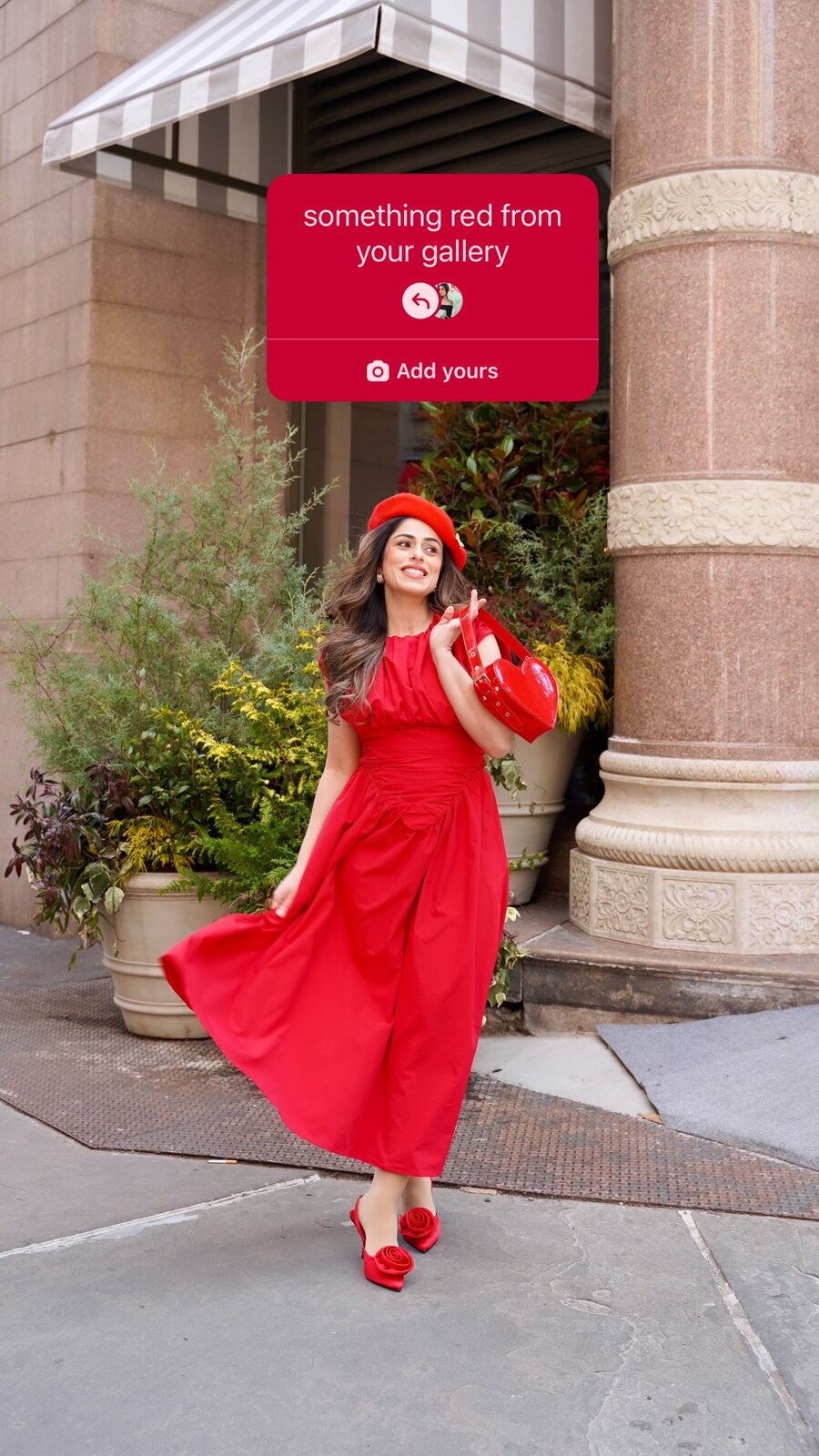 Roopsi Bansal walking down a city sidewalk in a red dress, red beret and red shoes holding a red heart-shaped bag