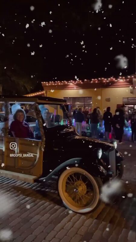 An antique car parked on a cobblestone street decorated with Christmas lights and fake snow in St. Augustine, Florida at night