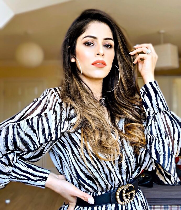 Standing with hands on hips wearing a black and white zebra-print wrap dress with a pearl-embellished Gucci belt and hoop earrings