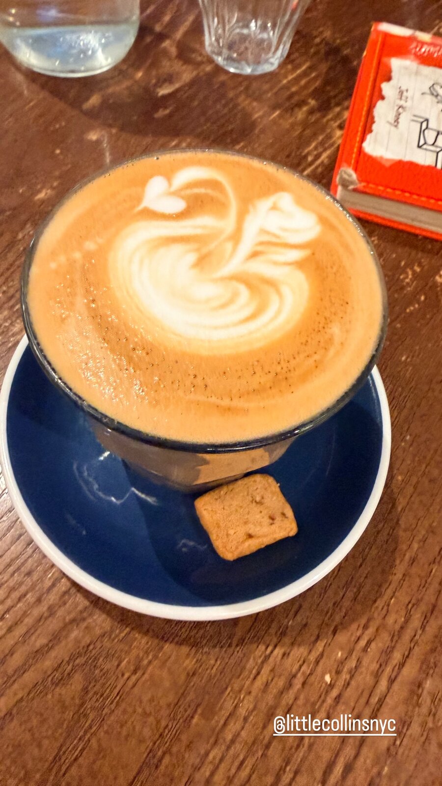 A latte with swan-shaped latte art and a butter cookie on a blue saucer at Little Collins NYC