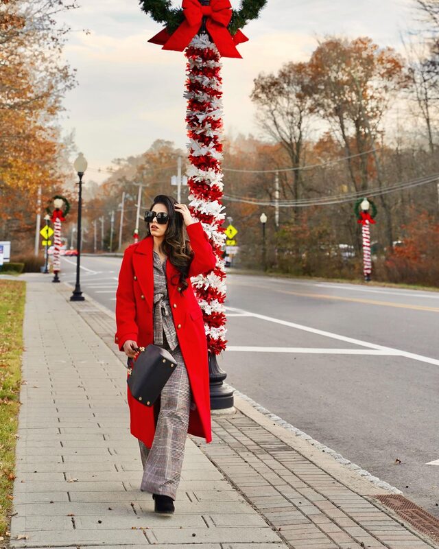 Roopsi Bansal in a red coat from Express walking a street decorated with candy-cane light poles for the holidays