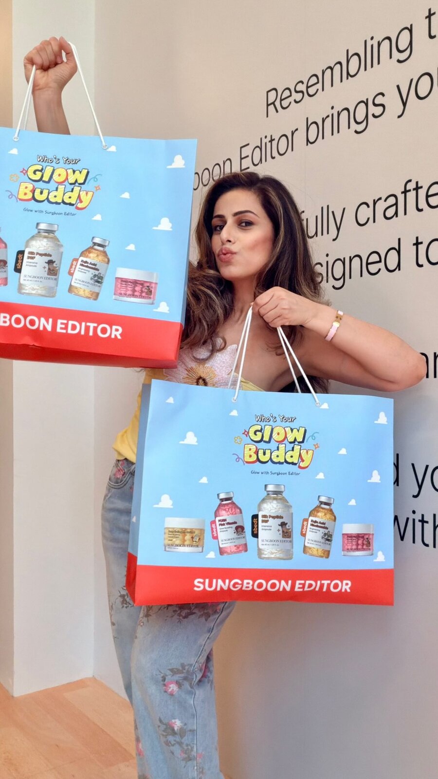 Roopsi Bansal holding up two more Sungboon Editor 'Who's Your Glow Buddy' gift bags filled with skincare ampoules and jars, at the Toy Story-themed popup