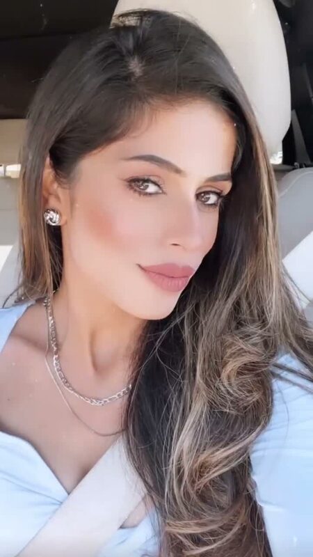 Close-up of Roopsi Bansal in a cream bow-neck blouse, one hand in her hair, taking a selfie inside a car