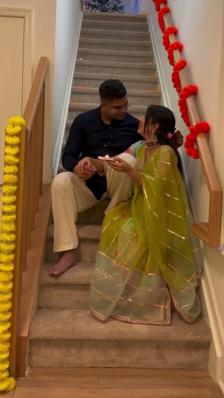 Roopsi Bansal and her husband performing an aarti on a staircase decorated with marigold garlands for Diwali