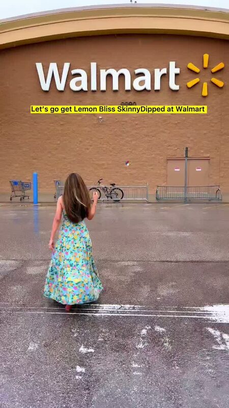 Roopsi Bansal in a pastel floral tiered maxi dress, walking toward a Walmart storefront with the text overlay 'Let's go get Lemon Bliss SkinnyDipped at Walmart'