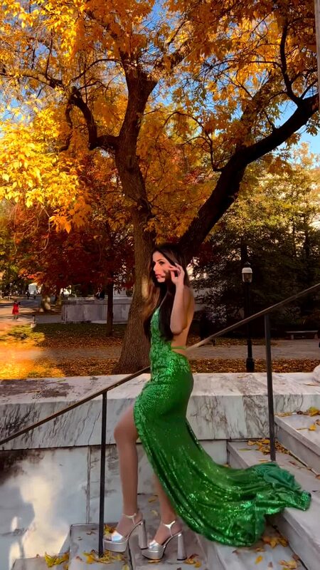 Roopsi Bansal in an emerald green sequined backless gown with a train, seated on marble steps under a golden maple tree