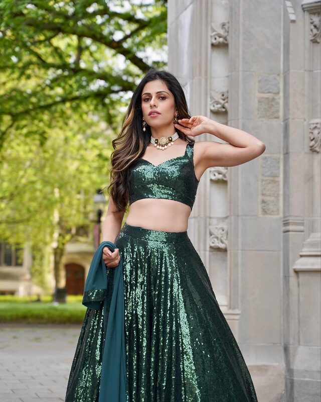 Roopsi Bansal in an emerald sequin lehenga with a matching dupatta, standing between stone columns at Princeton