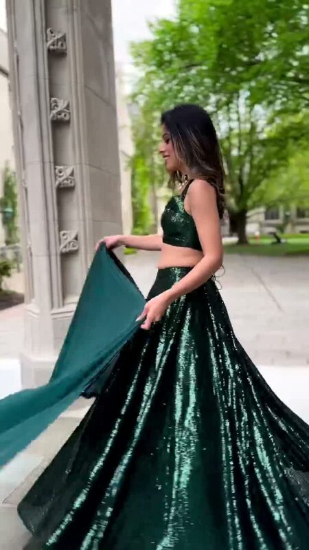 Roopsi Bansal in a sequin emerald green lehenga sweeping the train across a stone sidewalk at Princeton