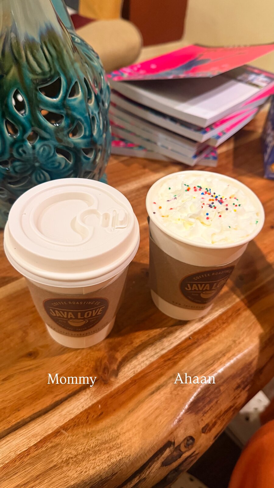 Two Java Love coffee cups on a wooden table, one plain and one topped with whipped cream and sprinkles