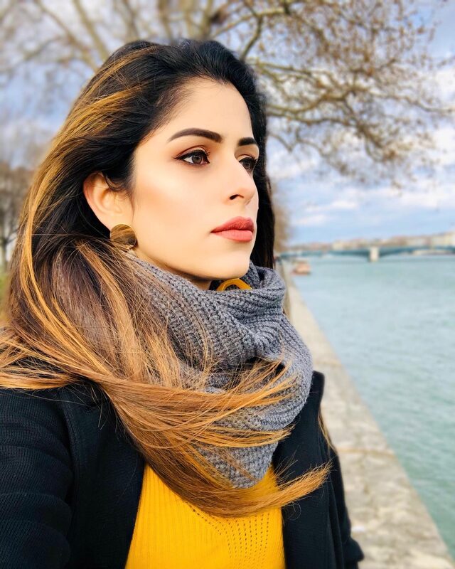 Close-up profile portrait by a river, wearing a mustard sweater, grey scarf, and gold hoop earrings, with warm smokey eye makeup and a red lip