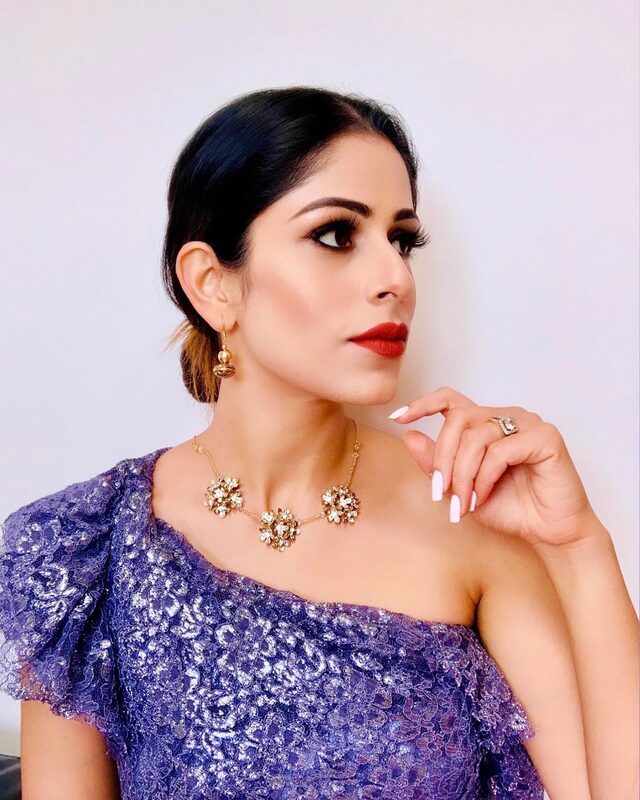 Roopsi Bansal wearing a purple lace one-shoulder top and a statement crystal necklace and earrings