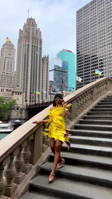 Roopsi Bansal in a yellow feather mini dress on the stairs of the Michigan Avenue Bridge, Tribune Tower in the background