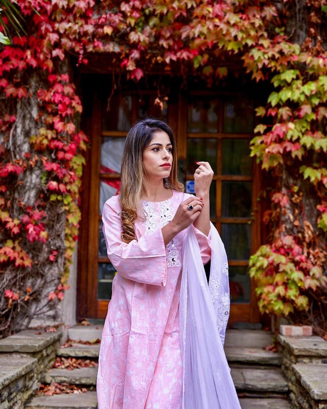 Roopsi Bansal in a pink embroidered kurta with a lavender dupatta, standing in an autumn doorway framed by red ivy