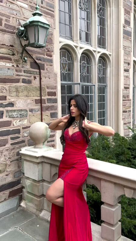 Roopsi Bansal in a red beaded gown with a thigh slit posed against Princeton's Gothic stone architecture