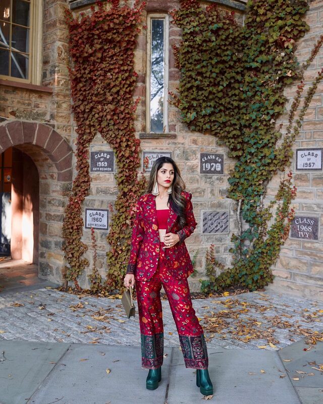Roopsi Bansal in a maroon printed blazer-and-pant set standing in front of an ivy-covered stone building with class reunion plaques in Princeton, New Jersey