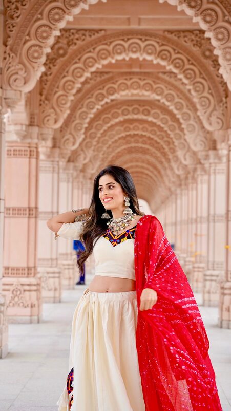 Roopsi Bansal in a white lehenga from Glamour Indian Wear USA and layered silver jewelry from Divakaari under the carved sandstone archways of BAPS Shri Swaminarayan Temple, Robbinsville, NJ