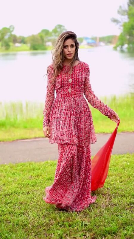 Roopsi Bansal in a red and white printed sharara set with a flowing red dupatta, standing on a path beside a lake in Florida
