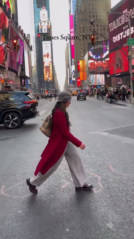 Roopsi Bansal in a red coat and cream trousers crossing the street in Times Square, New York