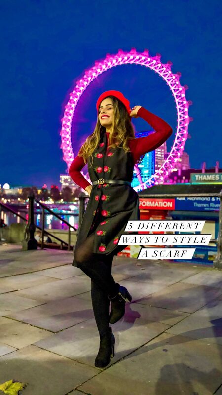 Roopsi Bansal in a red beret and a black rose-print scarf belted over a red top, posing in front of the London Eye lit up pink at night