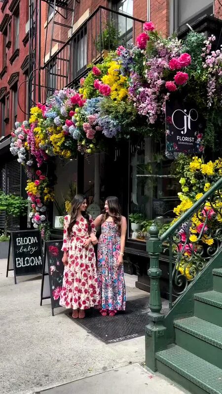 Roopsi Bansal and a friend in floral maxi dresses standing in front of a New York florist's storefront covered in colorful flowers