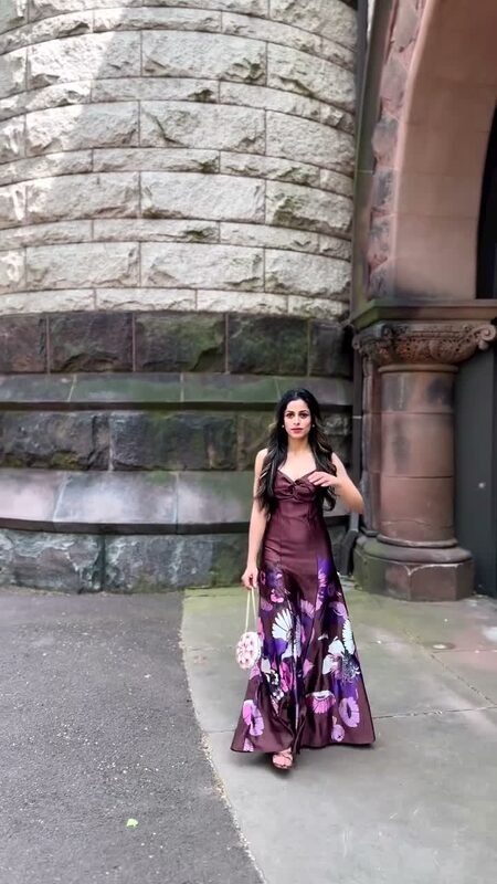 Roopsi Bansal in a satin floral twist-front maxi dress standing in front of a Gothic stone tower