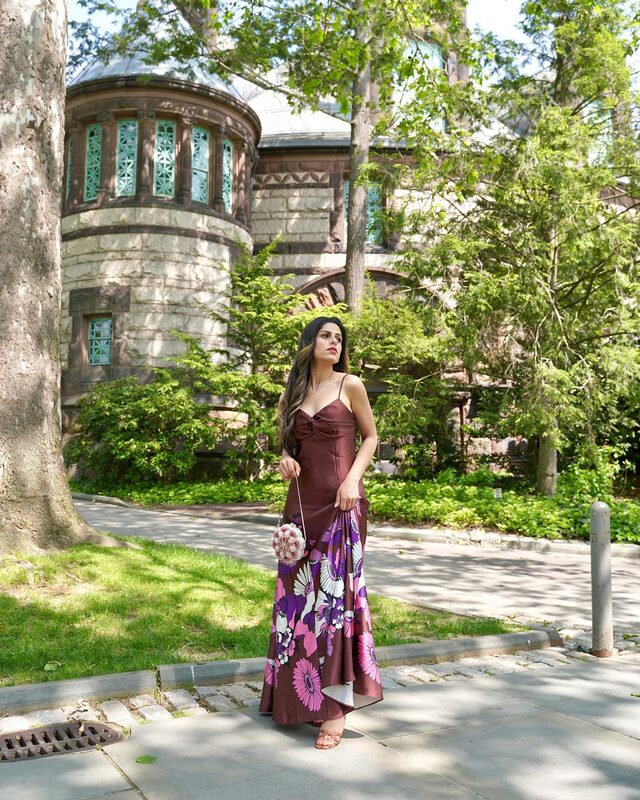 Roopsi Bansal in a floral-print satin slip dress standing in front of a stone turret with stained glass windows