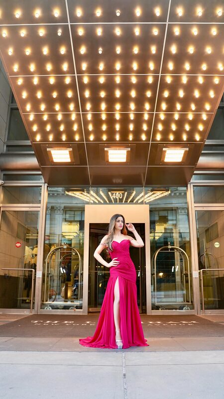 Roopsi Bansal in a fuchsia gown standing under the glowing marquee entrance of The Langham hotel in New York