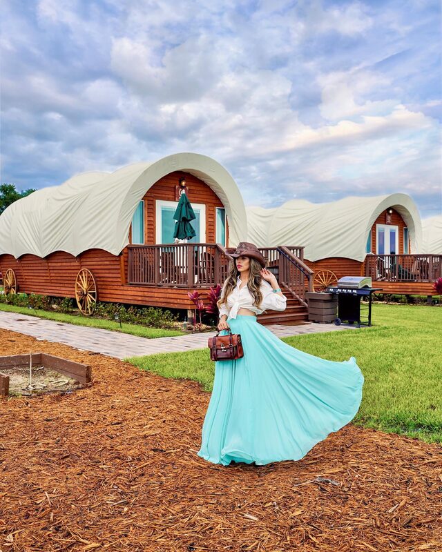 Roopsi Bansal in a green windowpane check midi skirt and white crop top, twirling on the deck of a tepee-shaped glamping tent named Roaming Buffalo at Westgate River Ranch Resort