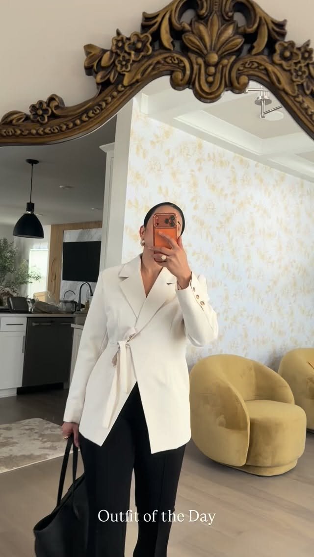 Roopsi Bansal taking a mirror selfie in a white wrap blazer and black trousers